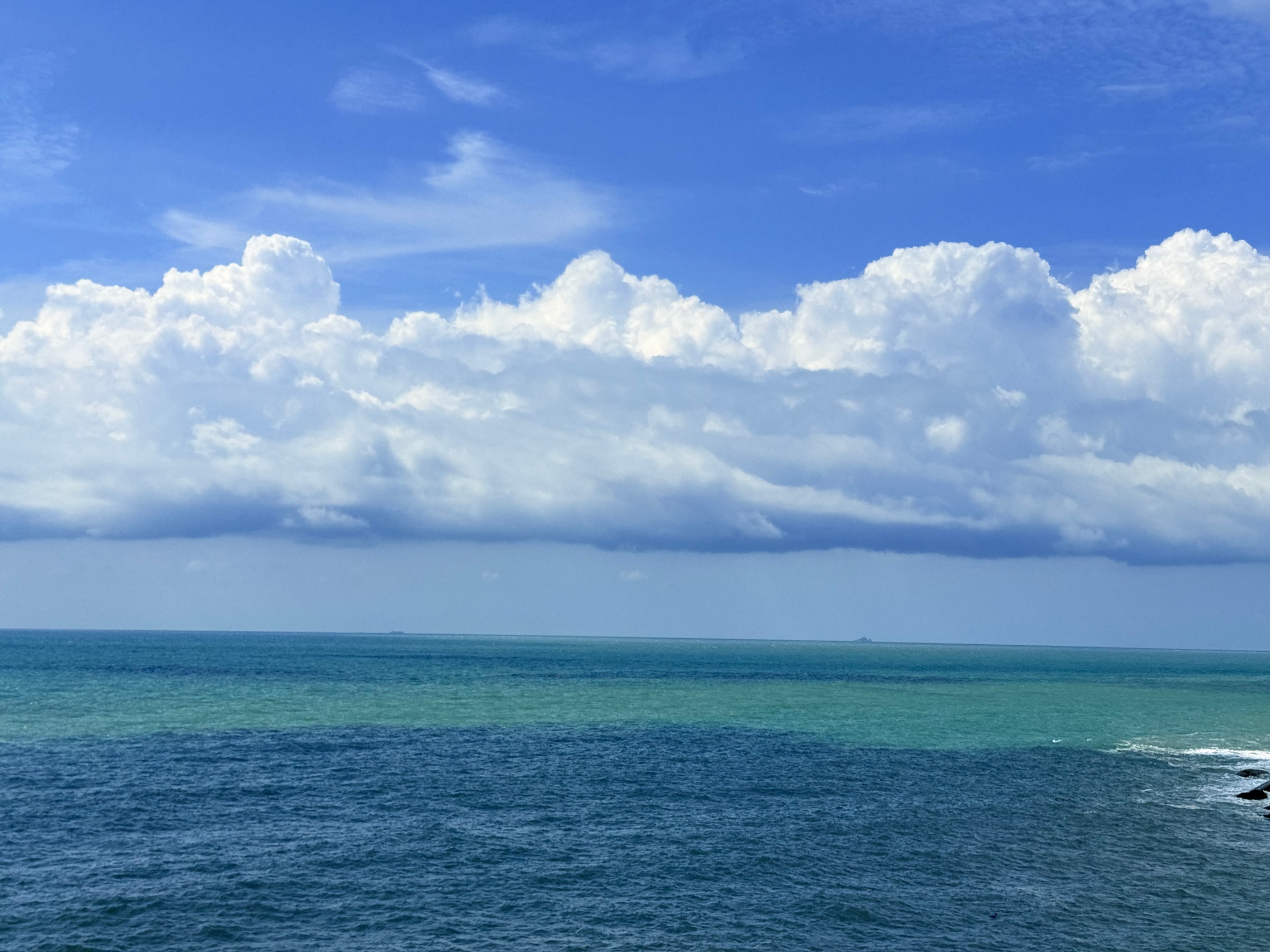 积云横在海平线上，海水分出深浅两种蓝。