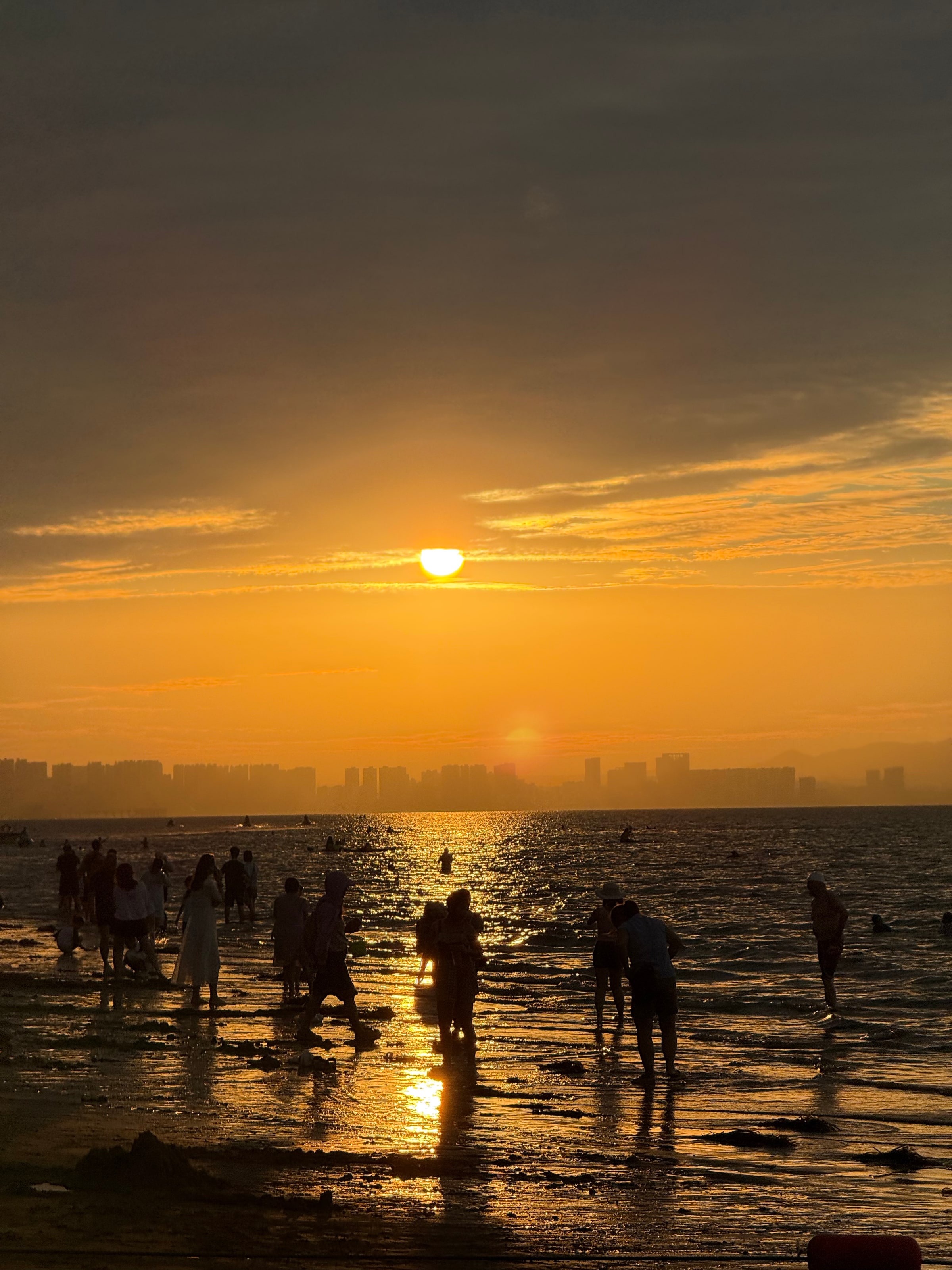 烟台的海滨日落，整片海面被夕阳镀成金色，人影成了剪影。